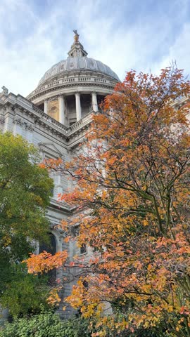 St Pauls Cathedral dome framed by vibrant orange autumn foliage under blue sky in London