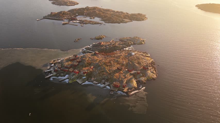 Aerial view of rocky islands with traditional red wooden houses and wooden docks surrounded by calm sea at sunset in Gothenburg, Vastra Gotaland Count, Sweden.