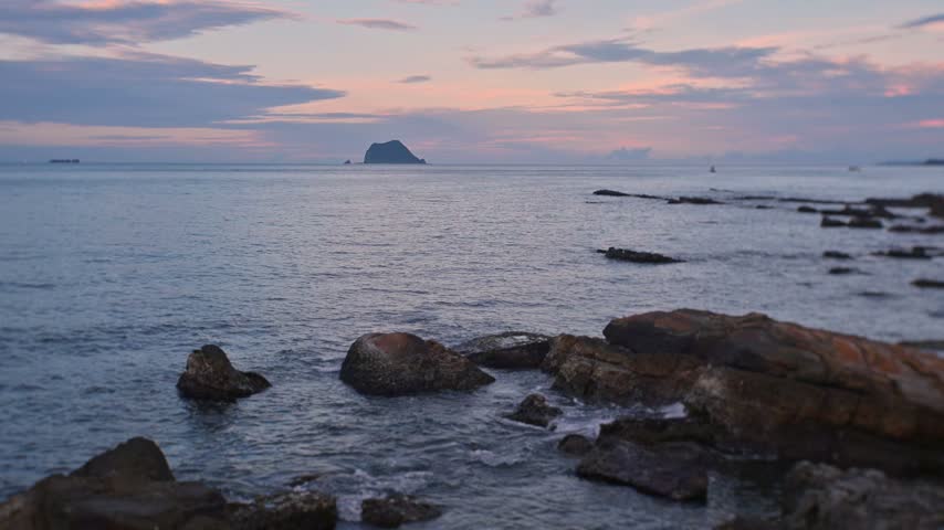 Scenic view of the ocean during dusk, featuring rocky shores in the foreground and Keelung Islet in the distance in Jinshan, New Taipei City, Taiwan.