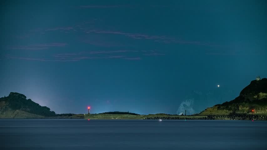 A glowing full moon rises in the night sky over the calm coastal sea with a distant boat and mountains in Jinshan, Taiwan.