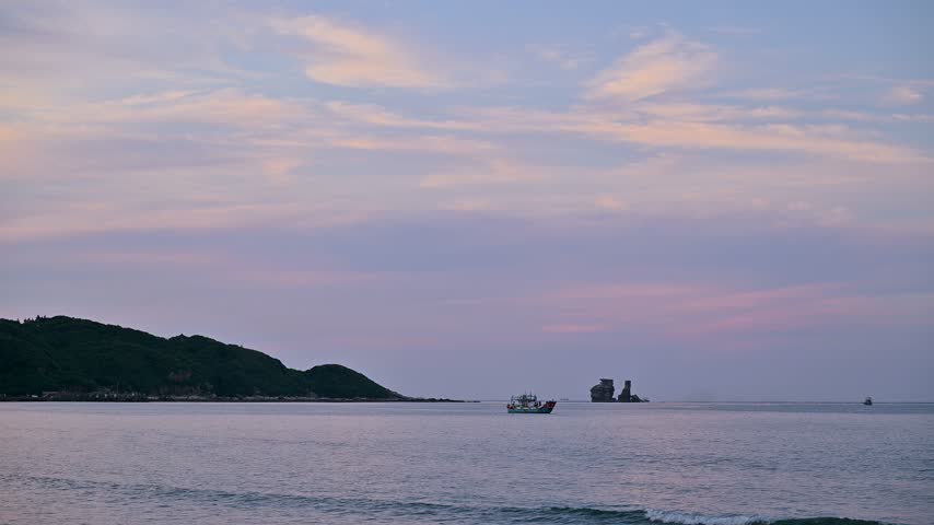 Scenic view of the coastline at Jinshan in New Taipei City, Taiwan, featuring a calm sea, rock formations, and a fishing boat under a colorful twilight sky.