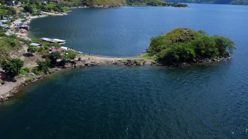 Aerial view of the lush green peninsula extending into the deep blue waters of Lake Toba in Parapat, North Sumatra, Indonesia.