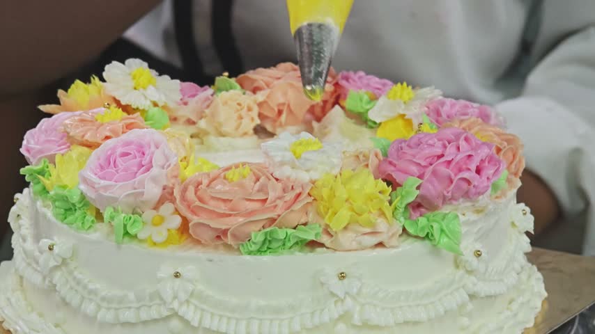 Piping yellow center details onto buttercream flowers for cake decoration.