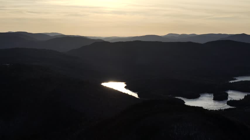 defaultAerial view of winding road along frozen lake in Quebec with forest and mountains under blue sky. g.