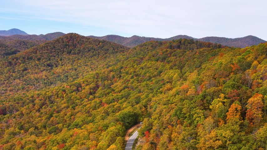 Peaceful roadside overlook in Tennessee Appalachians with parked car facing vibrant autumn scenery and endless forested mountain ridges.