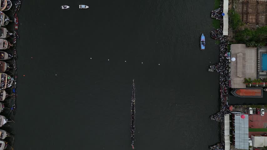 Vibrant cultural scene showing the annual Vallam Kali (boat race) in Kerala, India. Dozens of rowers chant and paddle a traditional wooden snake boat through the backwaters, showcasing India