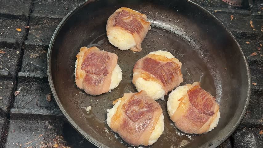 Grilled pork belly wrapped rice balls resting in a frying pan, top view of nikumaki onigiri at an izakaya kitchen in Japan