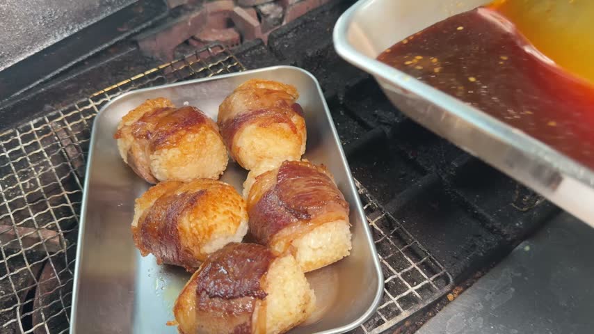 Pouring teriyaki sauce over grilled pork belly wrapped rice balls, glossy nikumaki onigiri at an izakaya kitchen in Japan