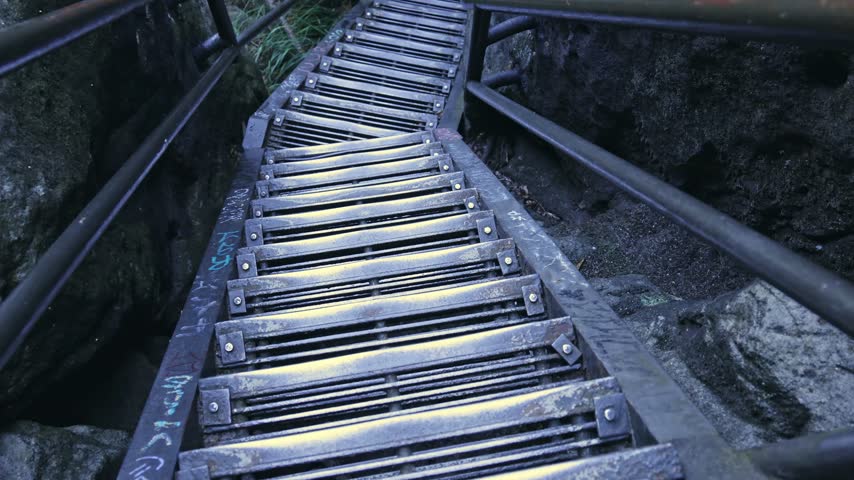 Metal stairs going down through steep rock formation in mountain forest