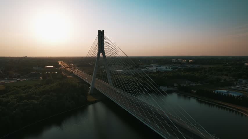 Aerial drone view of highway traffic crossing a large cable-stayed bridge over a river during a vibrant sunset.