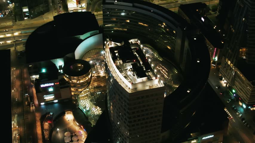 Aerial drone shot of Zote Tarasy shopping mall illuminated at night in Warsaw city center.