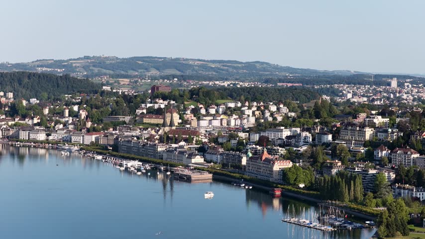 Aerial view of Lake Lucerne and the city waterfront, showing residential neighborhoods, marinas and green hills rising behind the shoreline in Switzerland.