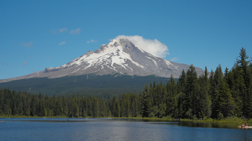 Mount Hood rises beyond Trillium Lake and evergreen forest beneath clear blue Oregon sky, medium establishing backdrop