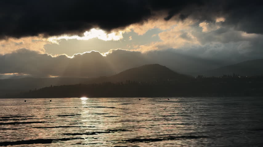 Sunset over the lake, with heavy cloud formations with light shining through an opening in the sky.