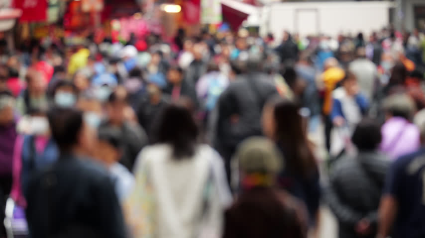 Blurred view, anonymous crowd of people walks along the busy pedestrian street of Kai Man Path in Tuen Mun. This daytime, out-of-focus shot captures local shoppers, some wearing face masks, moving past stalls to represent population density and everyday urban life in the Hong Kong