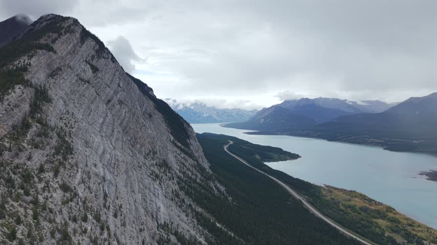 A sweeping view of a mountain ridge alongside the Saskatchewan River in Alberta, showcasing the lush green landscape and distant mountains under a cloudy sky.