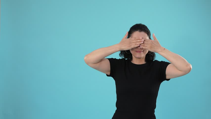 A woman covers her eyes, reveals her face, and expresses excitement and joy with open-mouthed laughter against a solid cyan background.