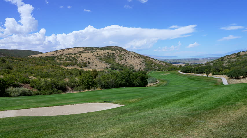 Panning view looking down the fairway of a golf course in summer looking past the sand trap.