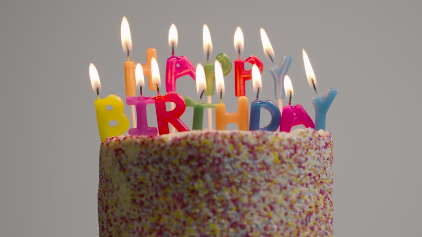 Close-up of a colorful birthday cake decorated with letter candles spelling Happy Birthday, with glowing flames and colorful sprinkles. Festive birthday celebration concept for parties, anniversaries, greetings and special occasions.