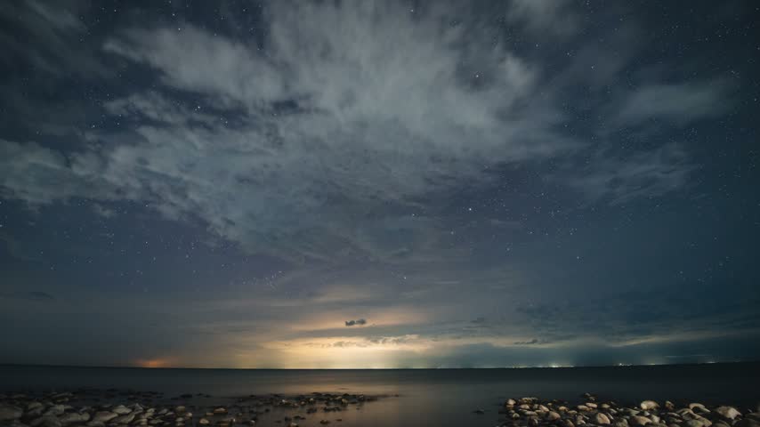 The Milky Way in the starry sky above Lake Issyk‑Kul, clouds are flying fast, lightning flashes on the horizon. timelapse