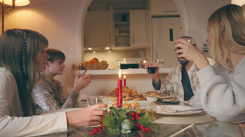 Family gathered at a festive holiday table, parents and two children sharing a cozy candlelit christmas ,thanksgiving dinner, talking, laughing and enjoying seasonal food together