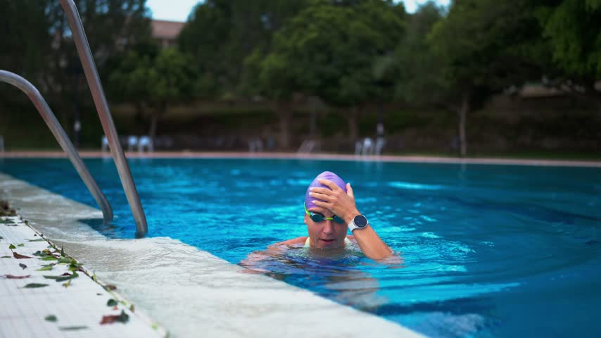 Athletic woman in a swimming cap adjusting her goggles in the blue water of an outdoor swimming pool, preparing for her intense training session for an upcoming competition