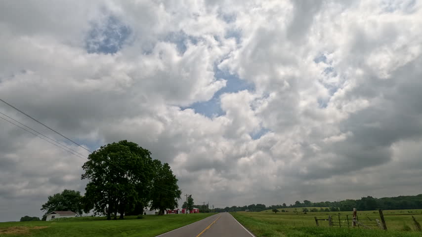 Road Trip Through Rural Southern Illinois. Car POV perspective driving through scenic Midwestern farmland past a bright red barn, storage silo, and farmhouse under an open sky. Located in Southern Illinois, USA.