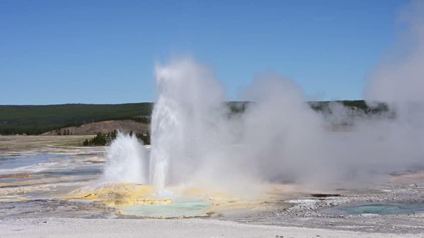 Clepsydra Geyser erupting with yellow minerals at base and small hot spring, sunny blue sky day, summer vacation at Yellowstone National Park viewing natural geothermal features
