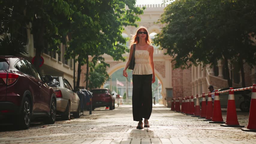 Joyful woman with sunglasses running towards the camera on a cobblestone street during a sunny day