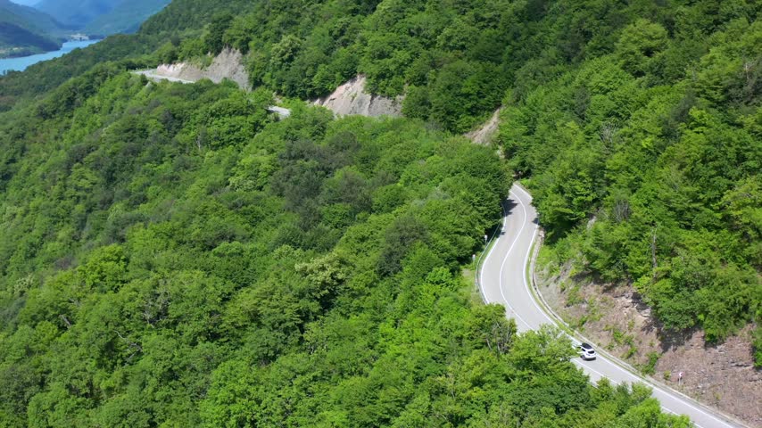Forest highway curves through aerial view along steep wooded terrain near Zhinvali Reservoir, supporting road travel, mobility planning, tourism promotion and mountain transport projects in Georgia.