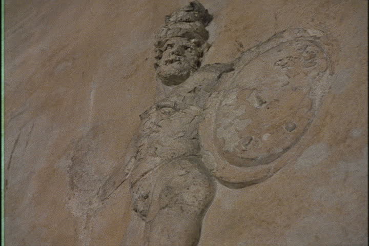 Push in to relief sculpture on wall, a man with a shield possibly Hercules in Naples, Italy.