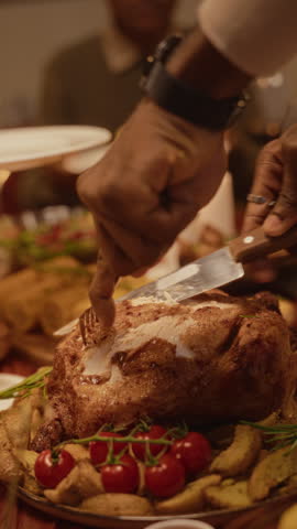 Vertical video of African American young adult carving roasted turkey during festive holiday feast. Footage represents culinary marketing campaigns and Thanksgiving dinner promotions