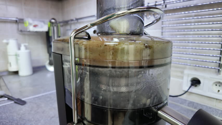 Close-up static shot of a modern electric juicer processing fresh green apples. The transparent container collects pulp and liquid while spinning under neutral indoor lighting with a blurred kitchen background.