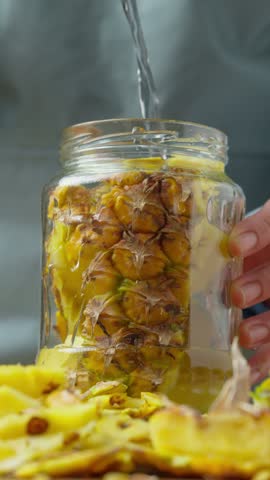 Pouring water over pineapple peels in a glass jar for fermentation
