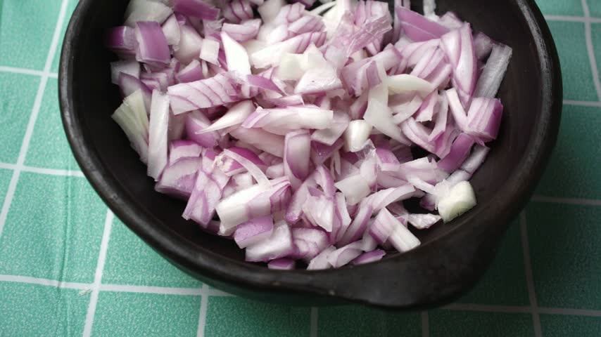 High angle panning shot of finely chopped red onion in a ceramic bowl
