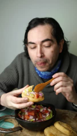 Close up view of a man eating golden sopaipillas topped with fresh pebre salsa, Man enjoying traditional Chilean fried sopaipilla bread with spicy tomato pebre