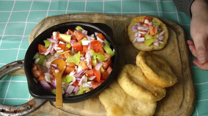 Close up of hands eating homemade sopaipillas with fresh tomato and onion pebre, High angle shot of hands enjoying fried sopaipillas topped with fresh pebre