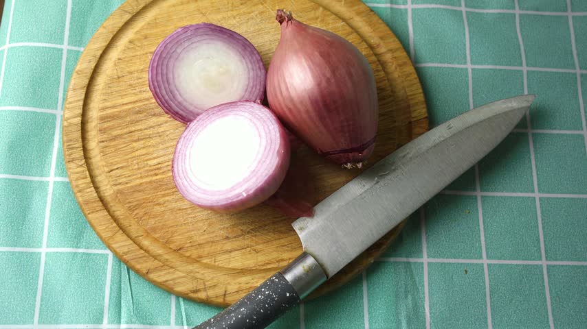 Close up view of a red onion halved next to a sharp knife on a wooden table