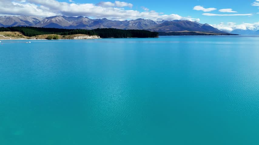 Aerial view of turquoise Lake Pukaki with mountain range and blue sky in New Zealand.