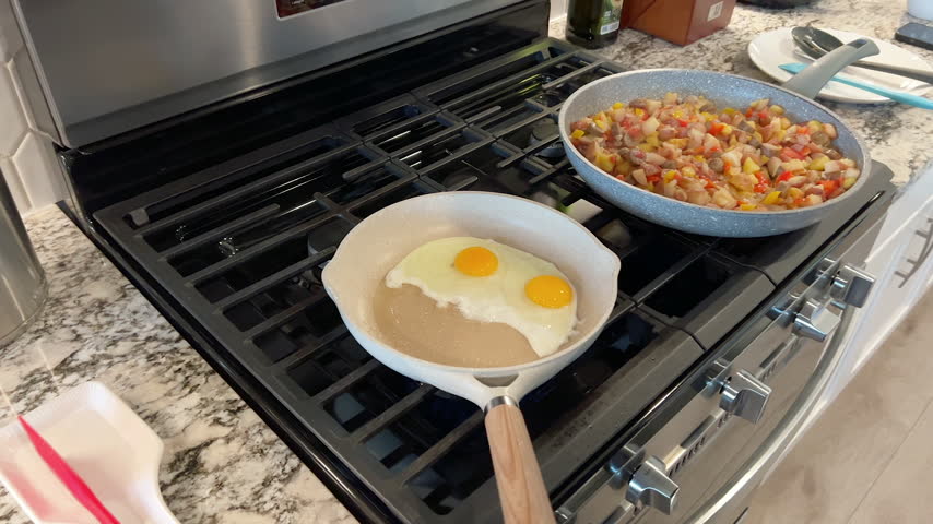 A person uses a red spatula to begin cooking an egg in a light-colored non-stick skillet. The egg white and yolk spread over the heated surface.