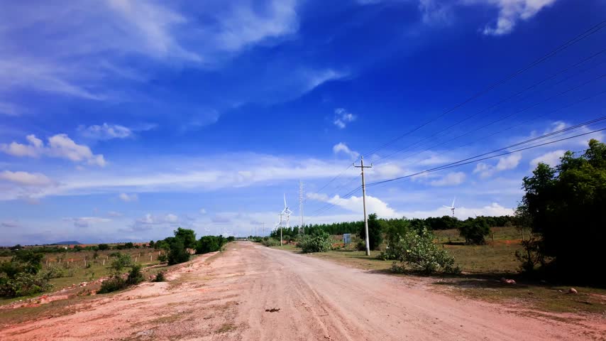 The sun shines bright over a dirt road in Hoa Thang, Lam Dong. Trees line the path while power lines stretch across the sky. This place shows the beauty of rural life in Vietnam.