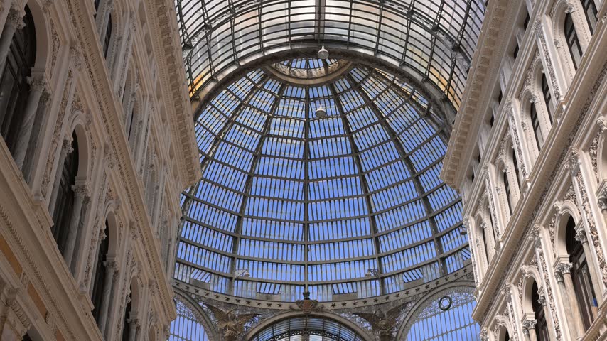 Upward view of the ornate glass dome roof and classical facades inside Galleria Umberto I in Naples.