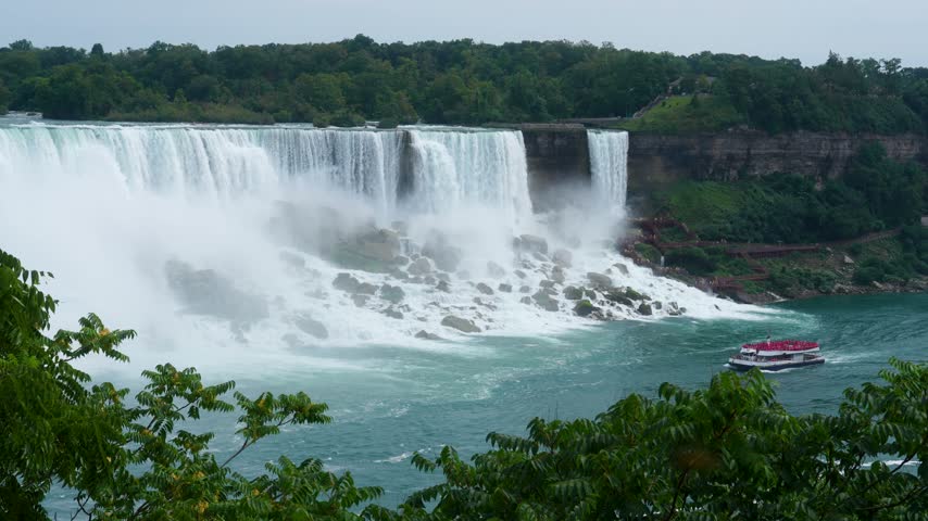 Niagara Falls framed by green leaves with tour boat crossing river, Canada