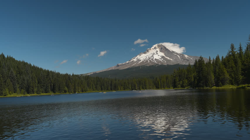 Snow-capped Mount Hood rises beyond Trillium Lake and dense Oregon evergreen forest, establishing pan right