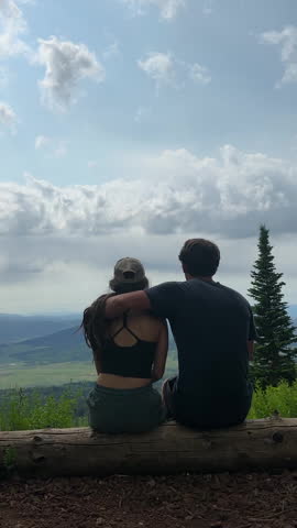 Woman and Man Sitting on Tree Trunk, Hugging and Kissing, Looking on Stunning Landscape of Rocky Mountains, Colorado USA