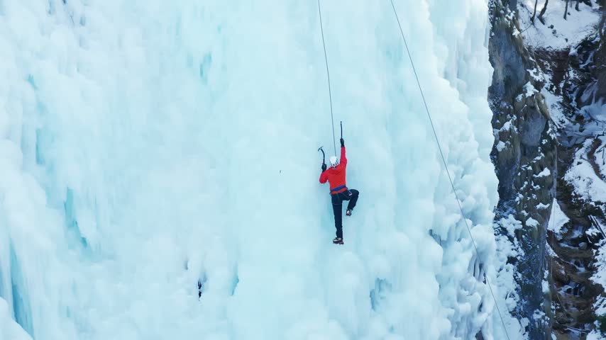 Aerial shot of a Caucasian ice climber facing a steep frozen wall, showcasing technical climbing, winter adventure, outdoor sport, and challenging icy terrain.
