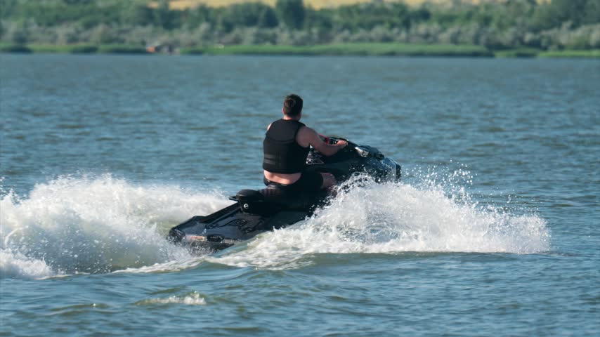 Person on personal watercraft speeding across calm lake surface. Active man in life jacket racing on jet ski during summer vacation, scenic nature background, dynamic water splashing.