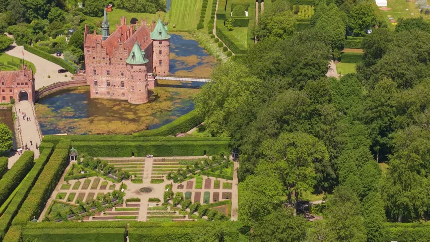 Smooth lateral drone flight captures Egeskov Castle and its distinctive geometric gardens, revealing elegant landscaping, symmetry, and the historic Danish estate.