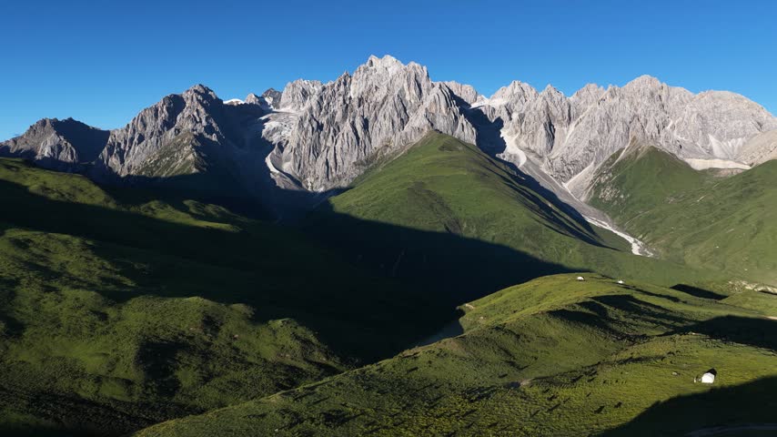 Landscape of green grassland and beautiful lake in high altitude mountain top, with snowcapped mountains in the distance	