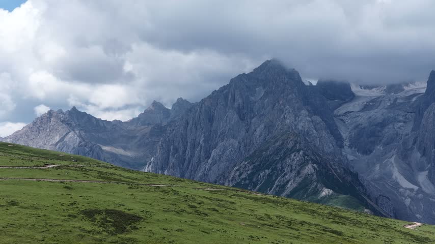 Landscape of green grassland and beautiful lake in high altitude mountain top, with snowcapped mountains in the distance	